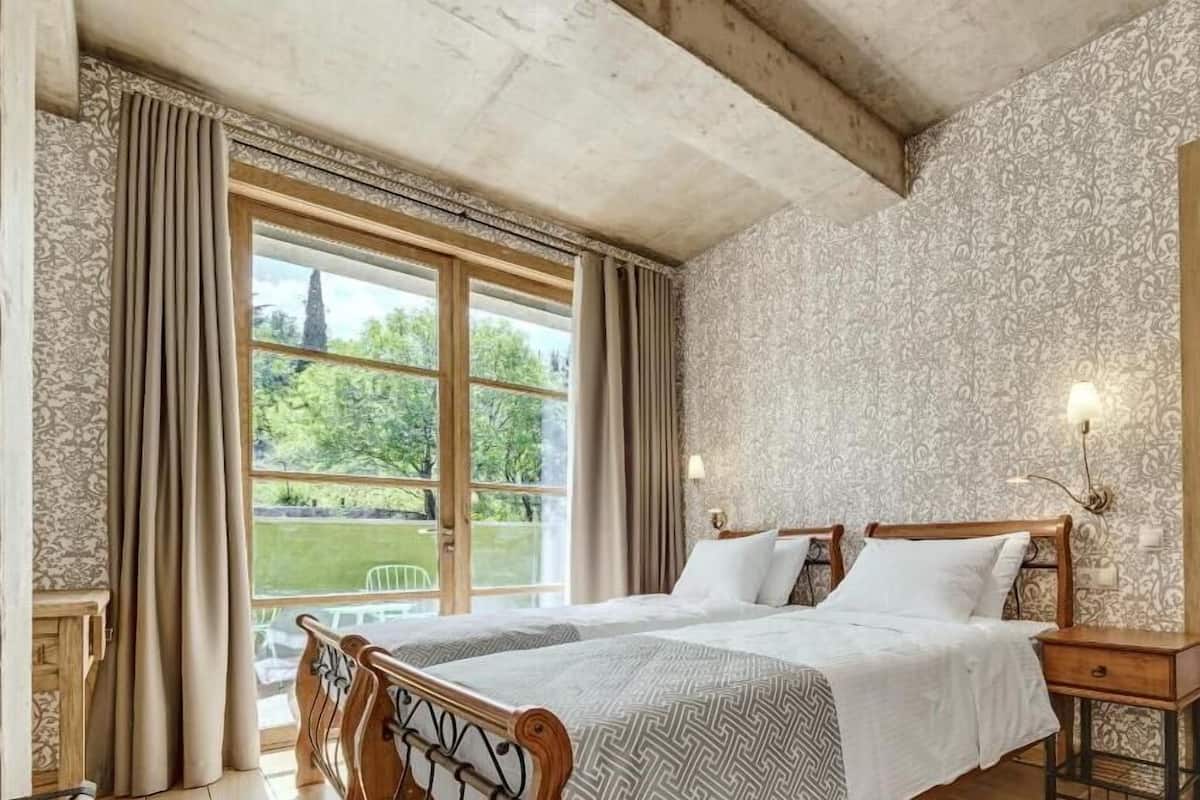A bedroom with a large bed, wooden headboard, and a view of a garden through a window.