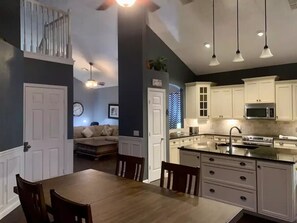 A modern kitchen with white cabinets, a stainless steel microwave, and a built-in oven. There is a dining area with a wooden table and chairs. - Awesome 6BR Vacation Home with a Pool (Kissimmee)