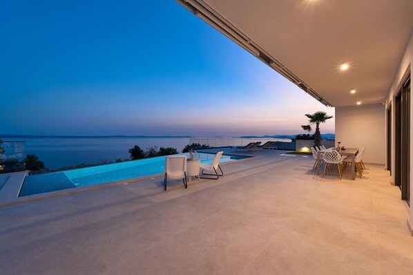 Eine moderne Außenterrasse mit Pool, Sitzgelegenheiten und Meerblick.