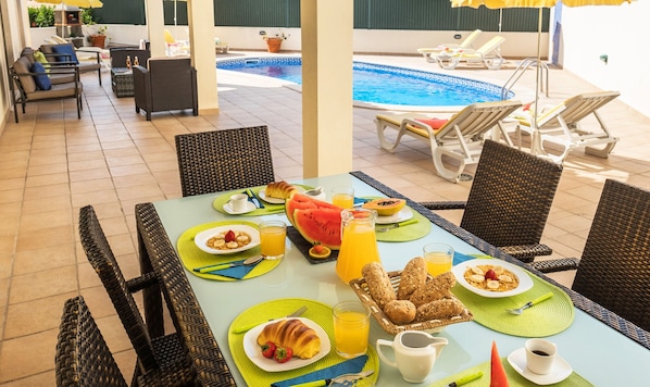 A breakfast setup with a pool view, wicker furniture, and a sunny outdoor setting.