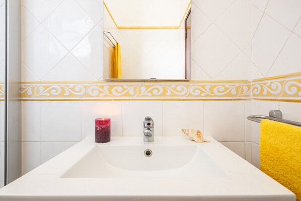 Un baño con un lavamanos blanco, un espejo encima y una toalla amarilla colgada en un tendedero.