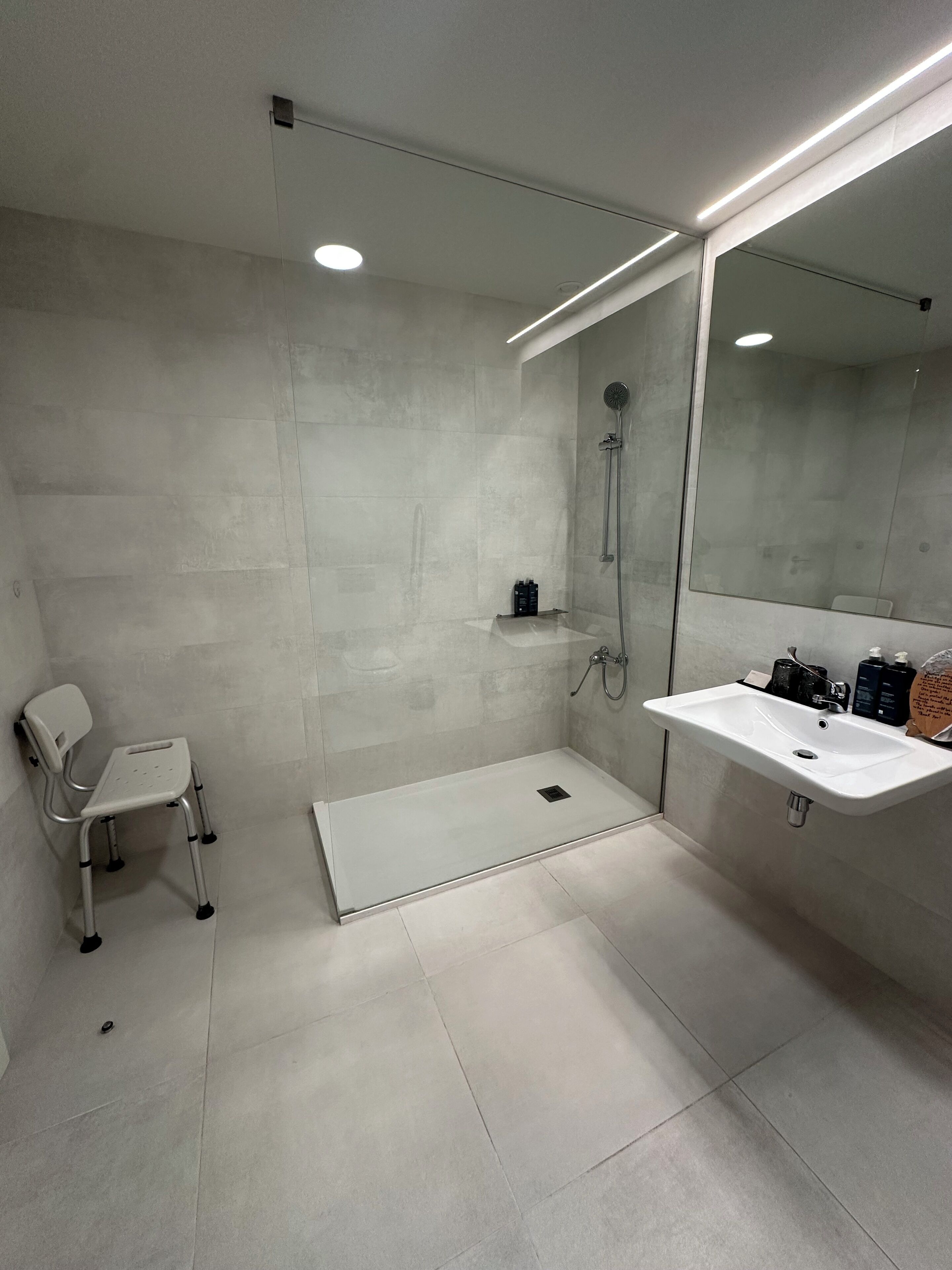 A modern bathroom with a walk-in shower, a white sink, and a chair.