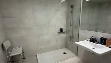 A modern bathroom with a walk-in shower, a white sink, and a chair.