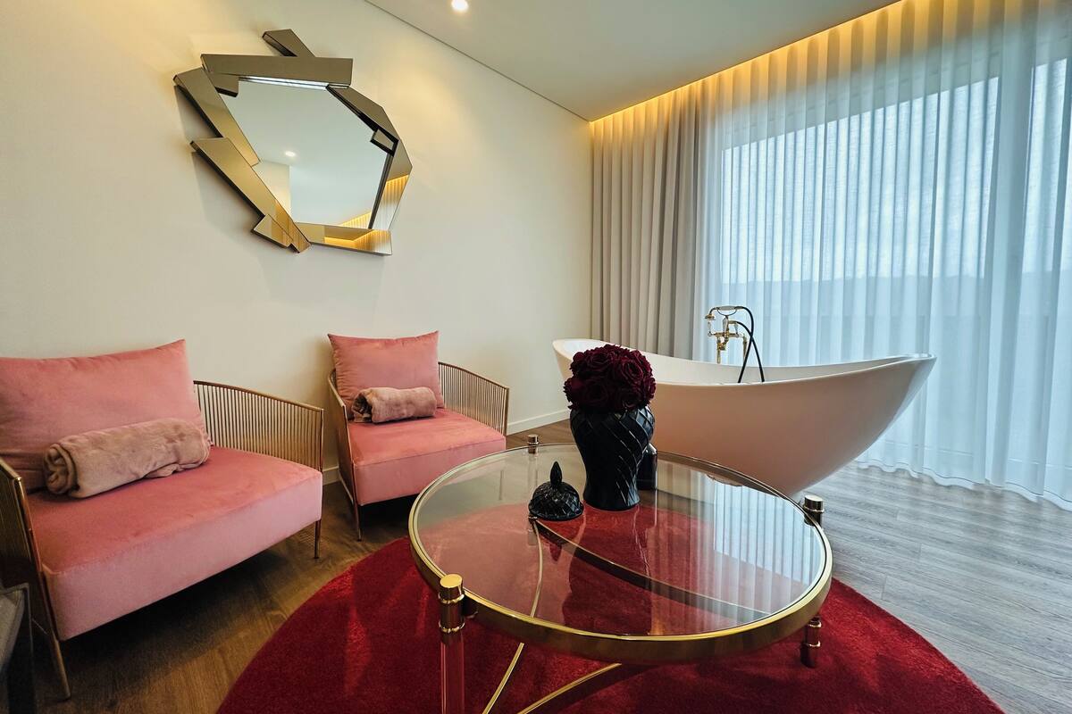A modern bathroom with a freestanding bathtub, a glass table, and two pink sofas.