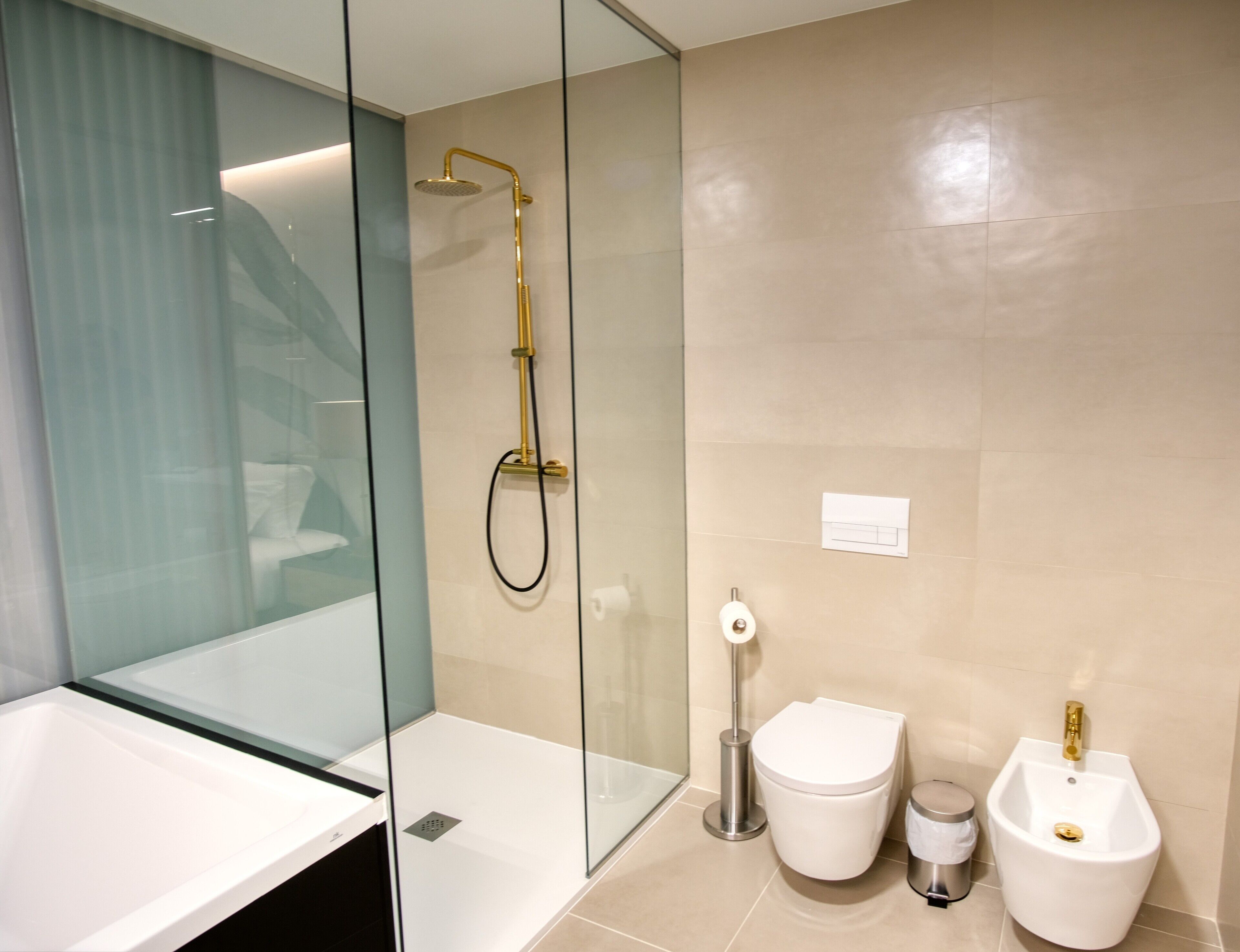 A modern bathroom with a glass shower enclosure, a white sink, a toilet, and a bidet.