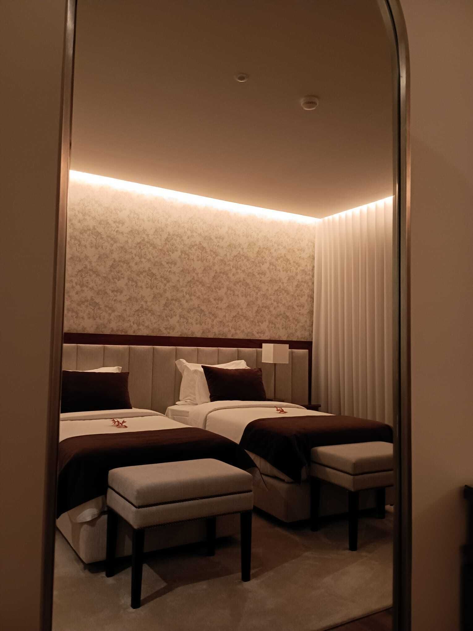 Een hotelkamer met twee bedden, een grote spiegel en verlicht plafond.