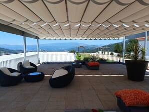 A covered outdoor seating area with chairs and a potted plant, overlooking a scenic view. - Hotel Cotto do Gatto (Ponte da Barca)