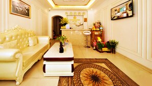 Un hall d’hôtel luxueux, avec un canapé blanc moelleux, une table basse, un comptoir de réception et un tapis décoratif.