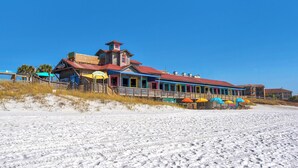 Un bâtiment situé en bord de mer, avec un toit rouge, de nombreuses fenêtres colorées et des espaces de repos extérieurs agrémentés de parasols.