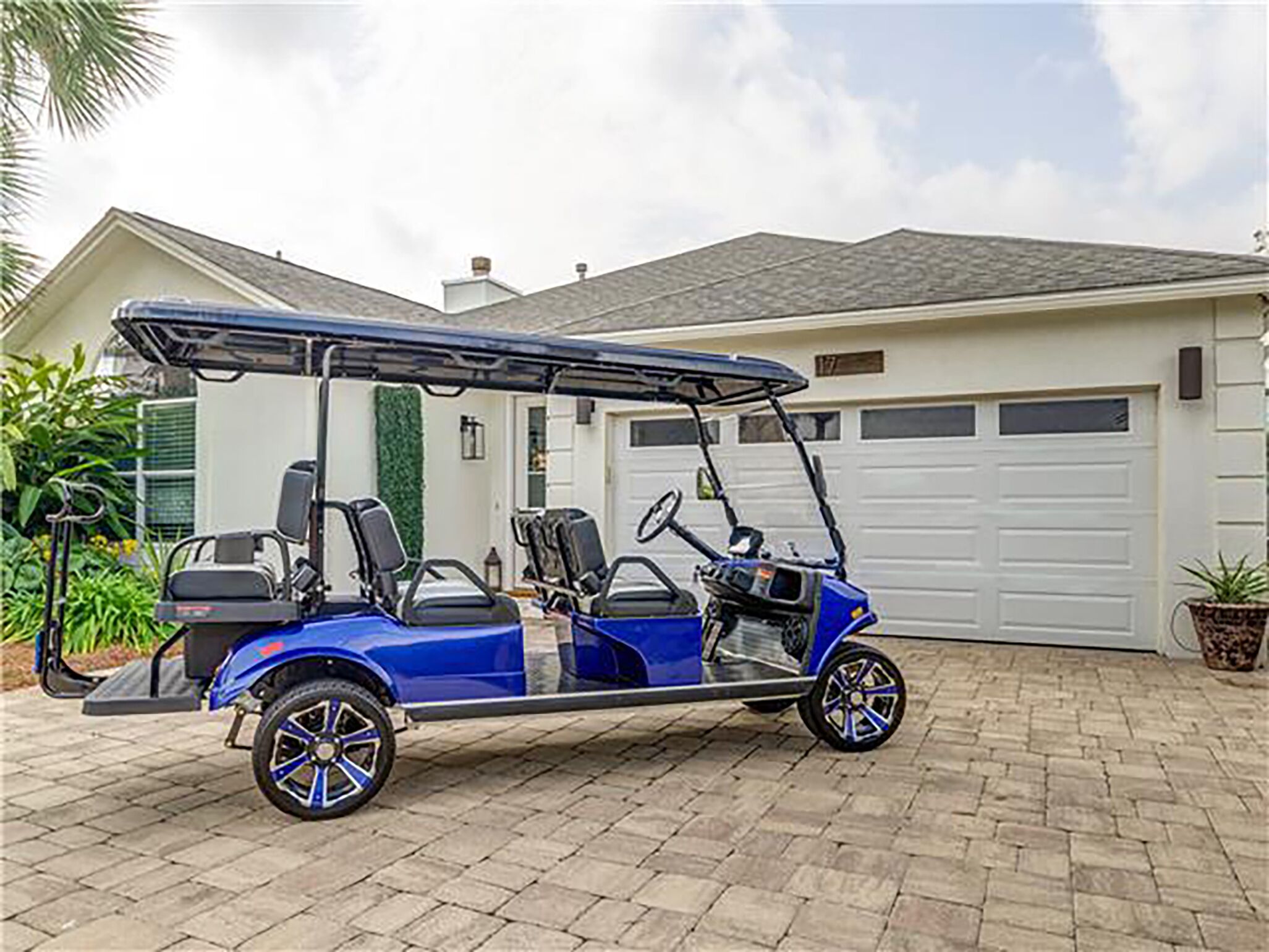 Une voiturette de golf bleue est garée devant une maison avec un garage.