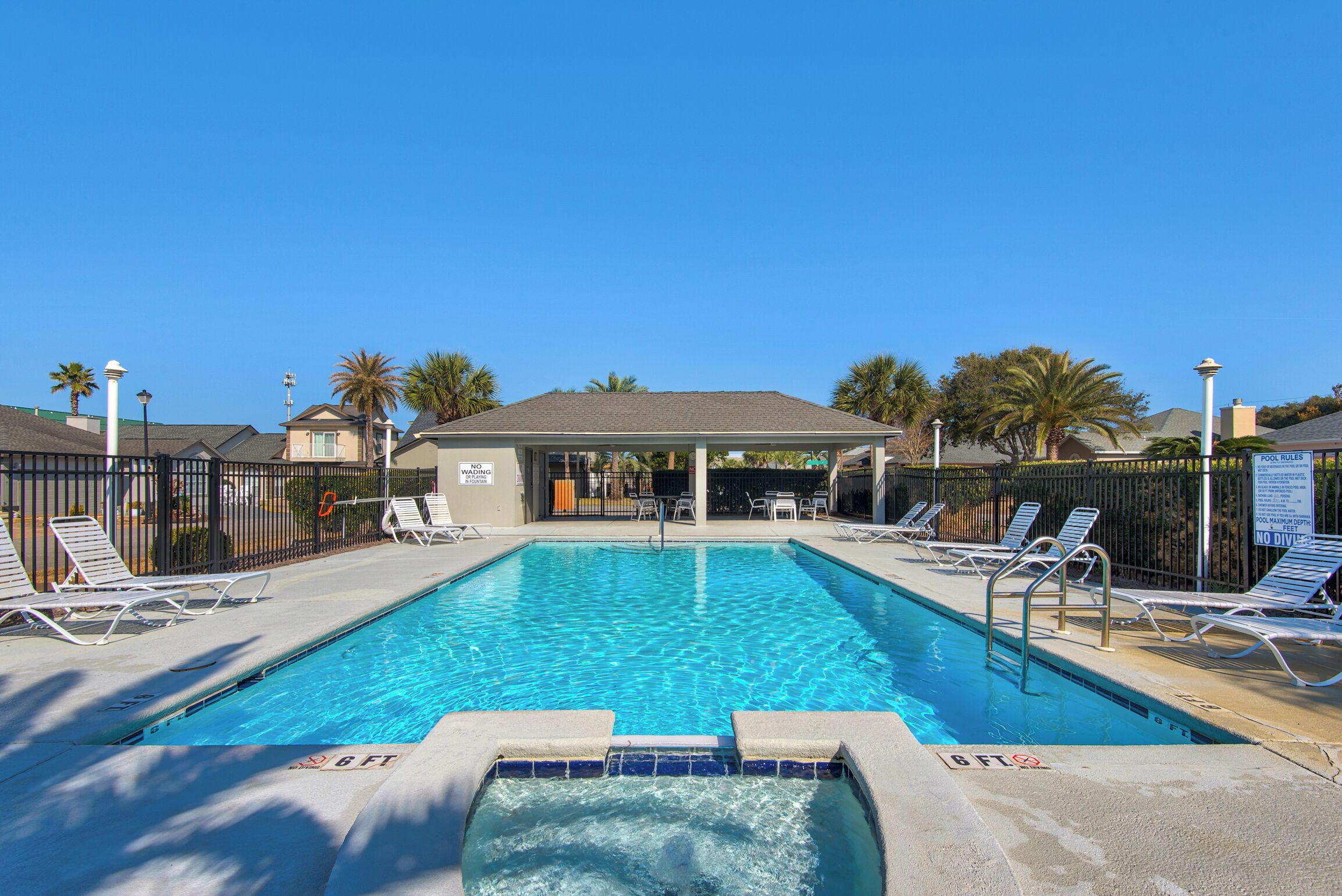 A rectangular swimming pool with a tiled edge, surrounded by lounge chairs and a fence.