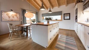 Una cocina con vigas de madera, una isla central, armarios blancos y una zona de comedor con sillas y mesa.