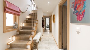Una escalera con acabado de madera, un banco al pie y una lámpara fijada a la pared.
