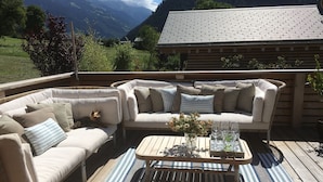 Un área de estar al aire libre con cubierta de madera, un sofá modular color beige y una mesa de centro con un florero.