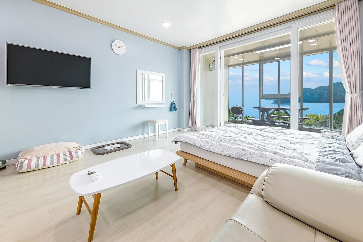 A bedroom with a bed, a TV, a window with a view, and a table.