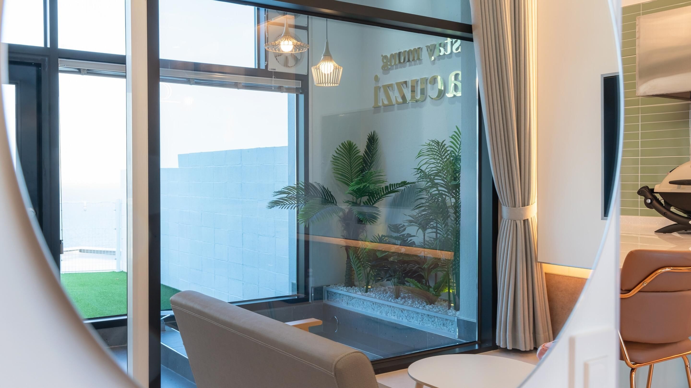A modern room with a glass wall, a seating area with a chair and table, and a decorative plant display.