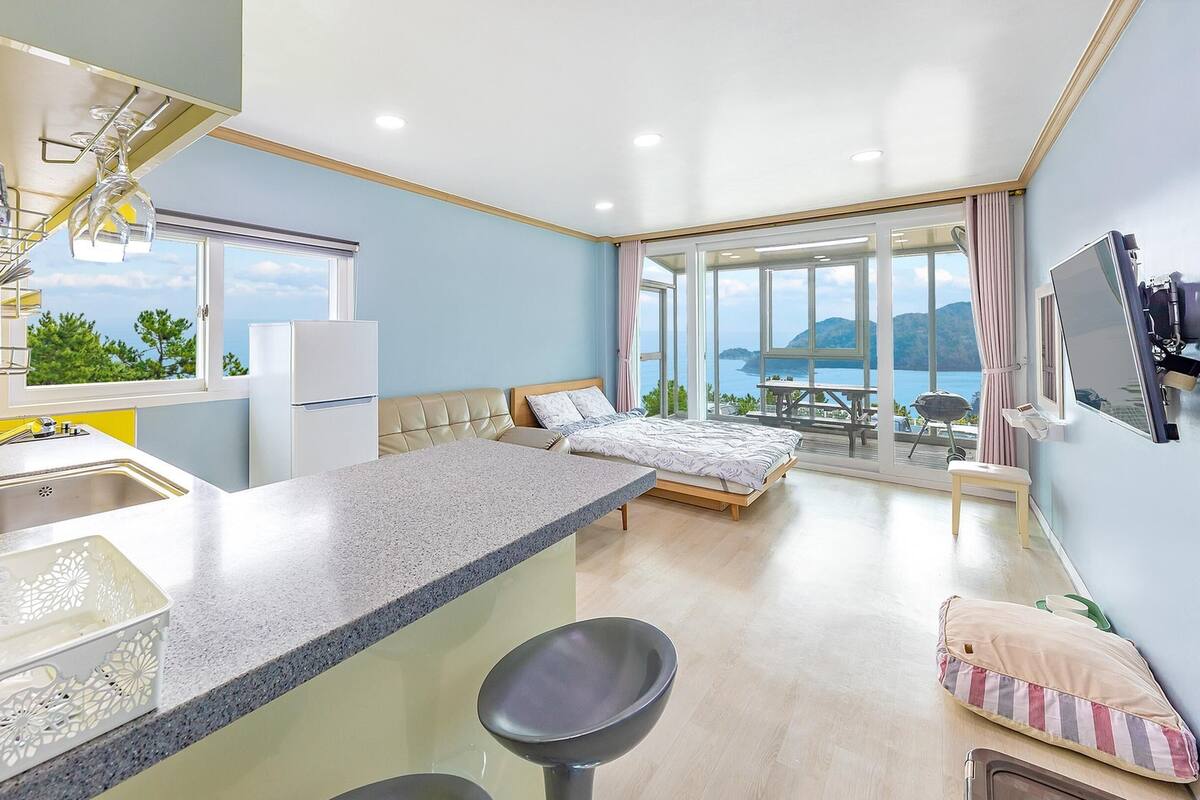 A modern kitchen with a large island, a dining area with a table and chairs, a bed with a view, and a bathroom with a mirror and sink.