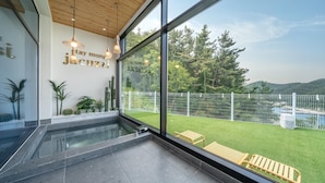 A modern interior with a large glass window, a wooden ceiling, and a view of a green lawn and white fence outside. - Yeosu Seuteimeong (Yeosu)