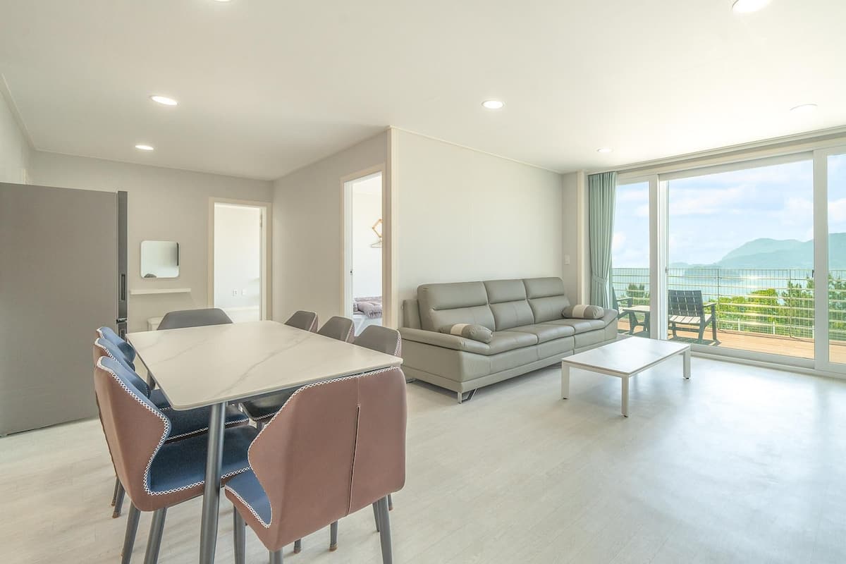 A modern living room with a dining area, a sofa, and a balcony with a view.
