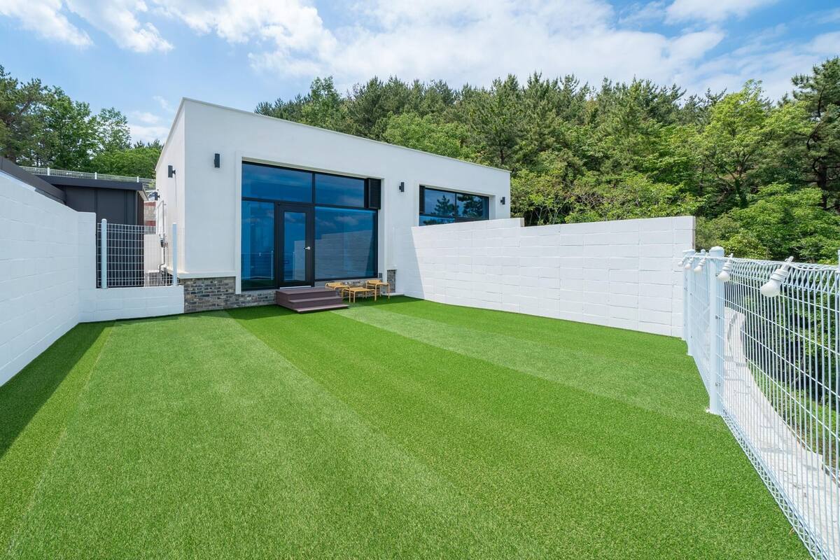 A modern house with a white exterior, large glass windows, and a well-maintained lawn.