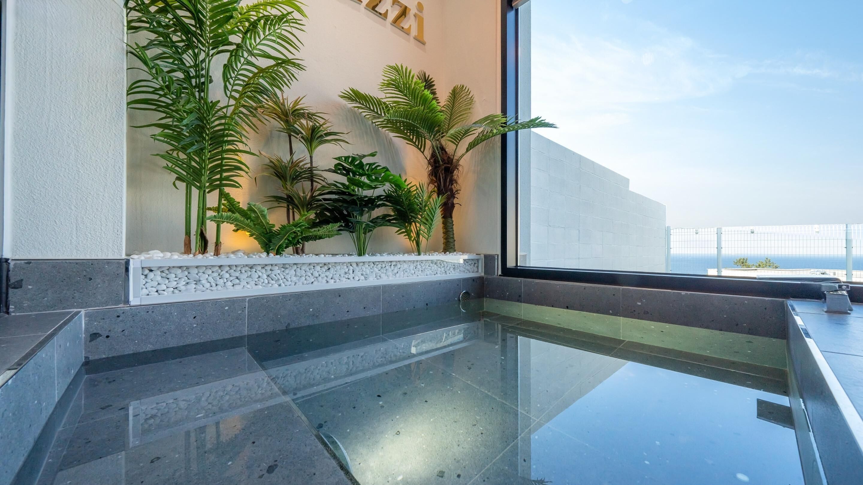 A modern indoor space with a glass floor, a white wall with a sign, and various green plants.