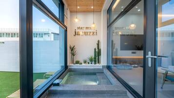 Une entrée moderne avec une porte en verre, un petit jardin intérieur agrémenté de cactus et un panneau indiquant : « profitez plus longtemps du jacuzzi ».