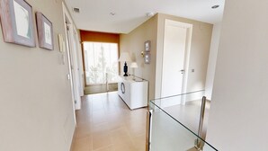 A hallway with a glass railing, a white door, and a window with a view of trees. - VILLA NIRVANA (El Perelló)