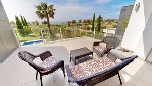 A balcony with wicker furniture, a pool, and a view of the sea and greenery. - VILLA NIRVANA (El Perelló)