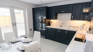 Een moderne keuken met donkere kastjes, een wit aanrecht en een eethoek met een tafel voor vier personen.