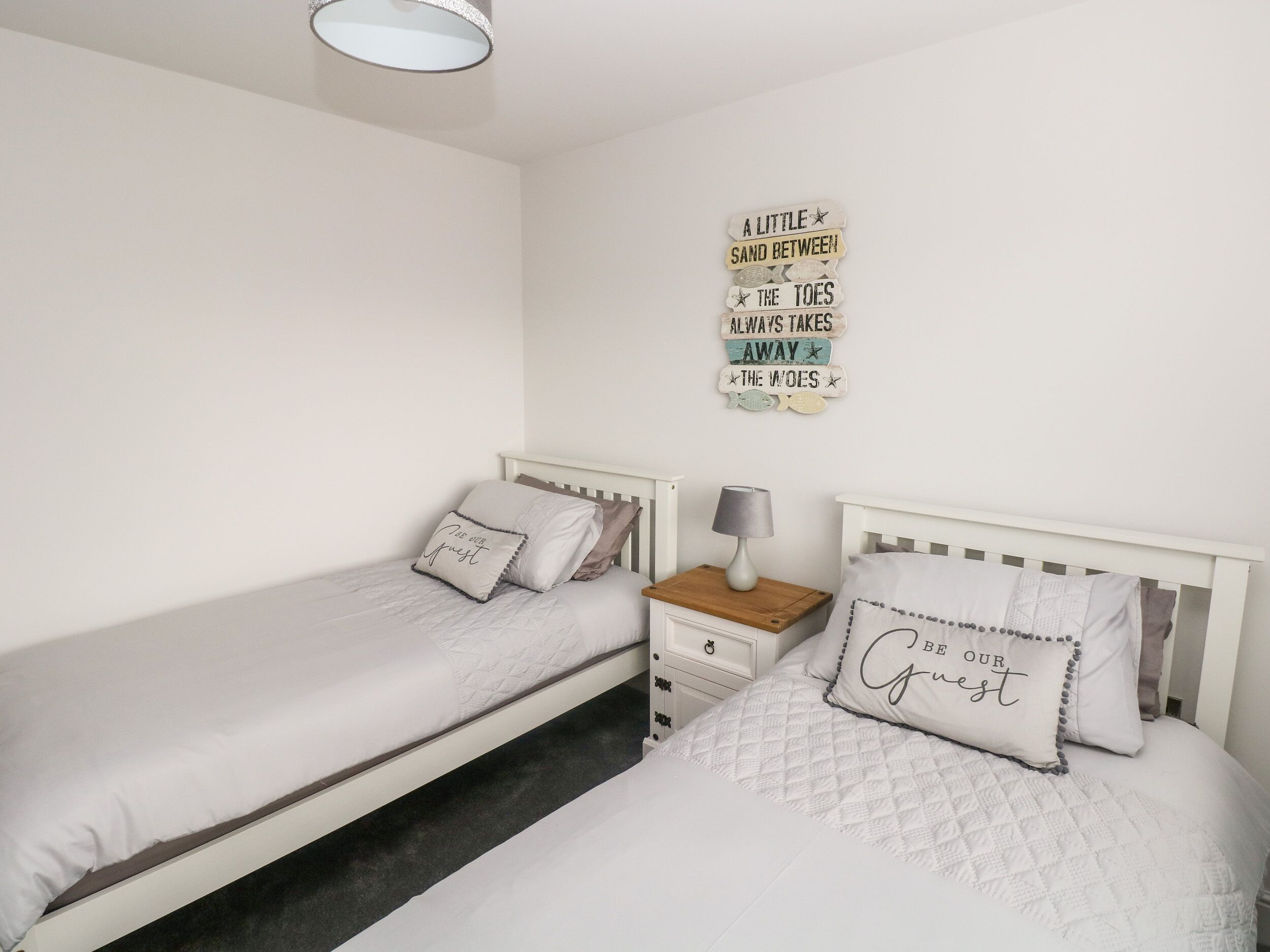 Un dormitorio con dos camas individuales, una mesita de noche con lámpara y un adorno en la pared.