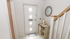Een hal met een witte deur, een houten kast met spiegel en een houten trap.