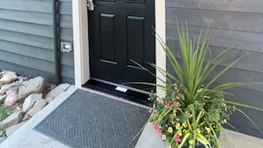 Een donkergrijze woning met een zwarte deur, een klein portaal en een bloembak met bloemen.
