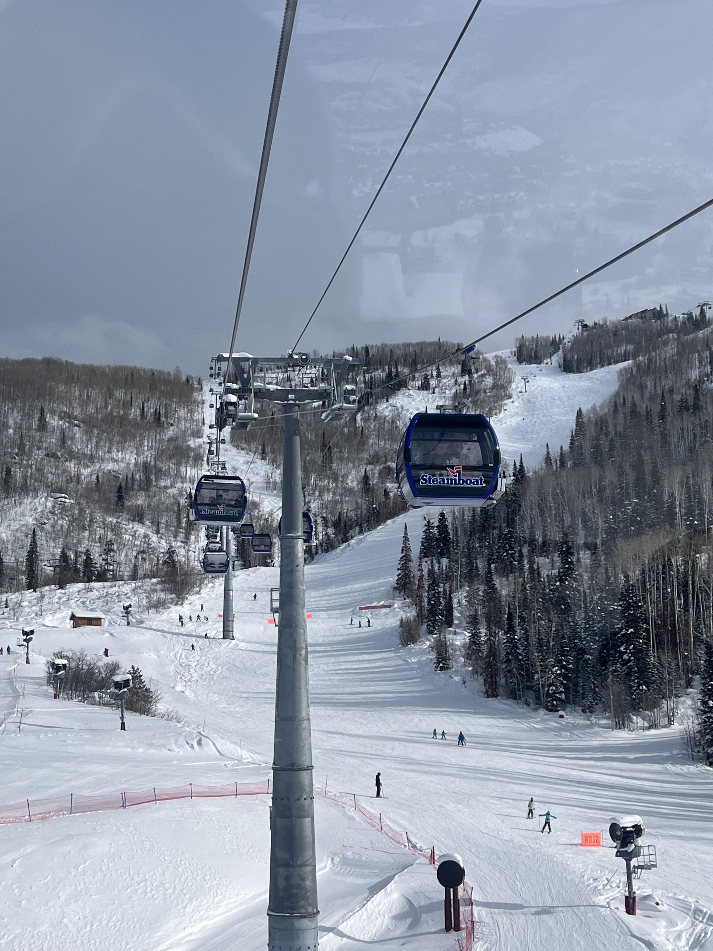 A ski lift with a sign indicating 'Steamboat' and a snowy mountain slope with skiers.