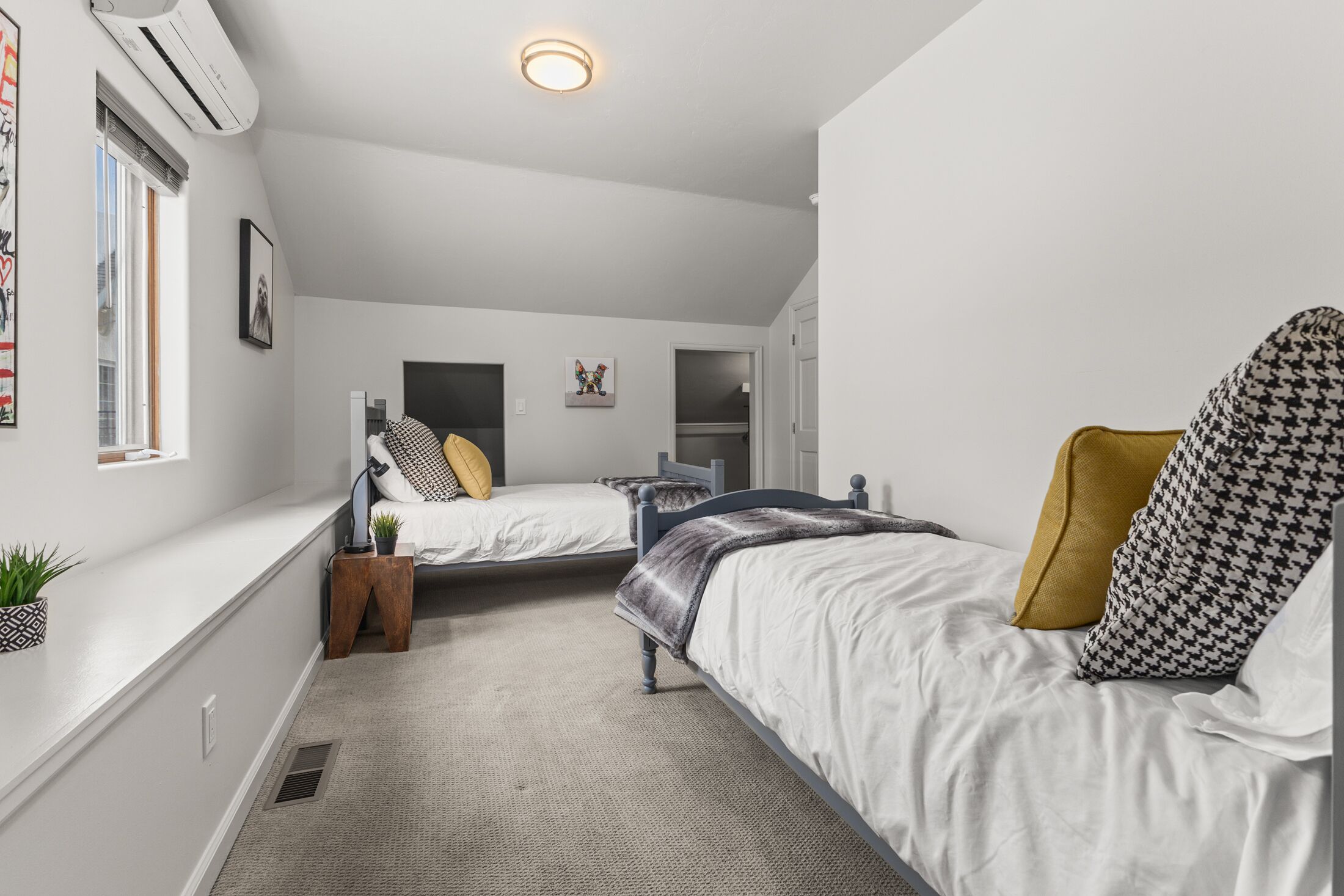 A bedroom with two beds, a window, an air conditioning unit, and a door.