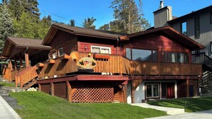 A two-story log cabin with a balcony, a wooden deck, and a well-maintained lawn. - Spacious private king suite steps to DT Banff (Banff)