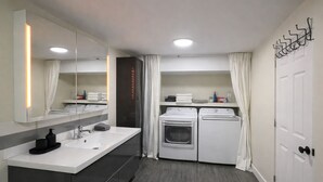 A modern bathroom with a large mirror, dual sinks, a shower, and a built-in washing machine. - Spacious private king suite steps to DT Banff (Banff)