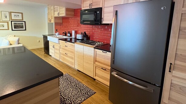 A modern kitchen with wooden cabinets, a black refrigerator, a microwave, and a clock on the wall. - Spacious private king suite steps to DT Banff (Banff)