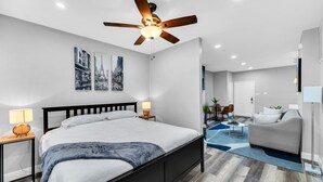 Une chambre moderne avec un lit, des lampes de chevet, un ventilateur de plafond et des œuvres d’art accrochées au mur.