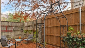 Un jardin avec une clôture en bois, un portail en métal, du mobilier d’extérieur et une plante en pot.
