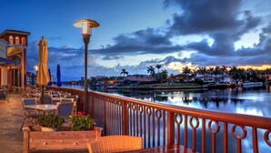 An outdoor patio with tables and chairs, a view of a body of water, and a building with a balcony. - Briarwood Vacation Home: Electric Heated Pool with Lake View - Naples, Fl  (Naples)