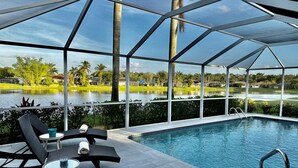 A pool area with a covered seating area, a pool, and a view of a lake and surrounding landscape. - Briarwood Vacation Home: Electric Heated Pool with Lake View - Naples, Fl  (Naples)
