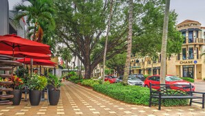 A paved walkway lined with palm trees and red umbrellas, leading to a building with a 'Chase' sign. - Briarwood Vacation Home: Electric Heated Pool with Lake View - Naples, Fl  (Naples)