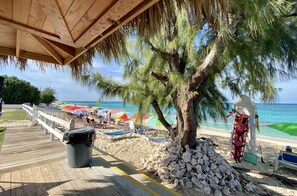 Une plage avec une terrasse en bois, une poubelle, un tas de rochers et des parasols de plage.