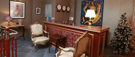 Una hall con una reception, due poltrone decorate, un piccolo albero di Natale e un grande quadro appeso al muro.