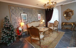 Een kamer met een bank, fauteuils, een bijzettafeltje, een kerstboom en een kroonluchter.