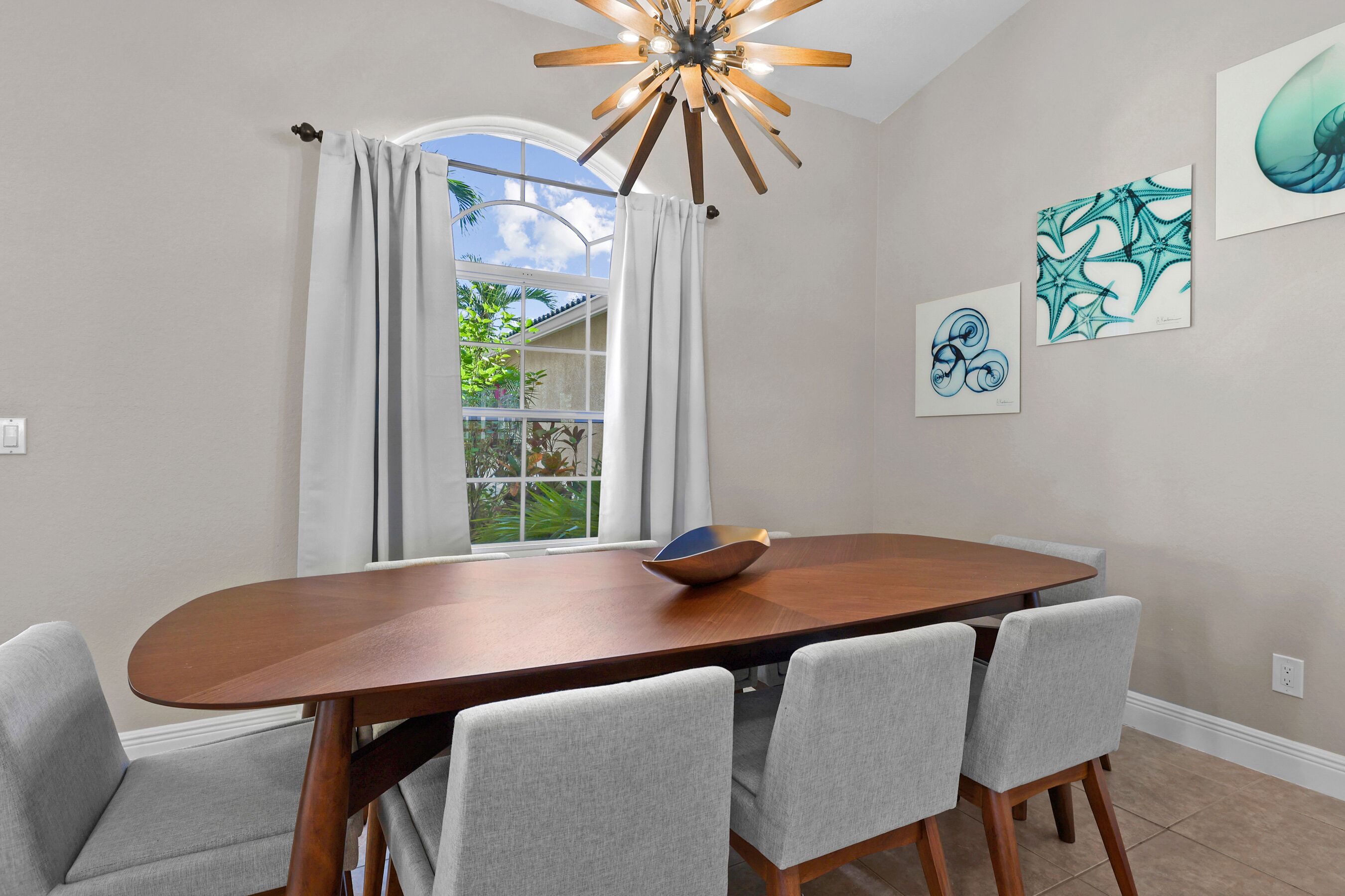 Un coin repas avec une table en bois, des chaises grises, un lustre moderne et des œuvres d’art accrochées aux murs.
