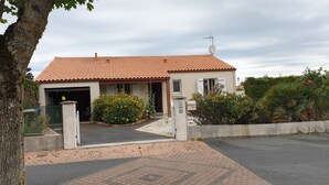A two-story house with a tiled roof, a garage, and a small garden with yellow flowers.