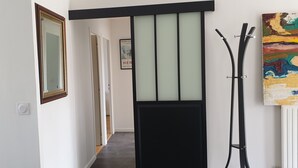 A hallway with a framed mirror, a door with frosted glass panels, and a coat rack with a painting on the wall.