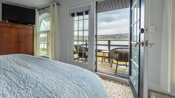 Une chambre dotée d’un grand lit, d’une armoire en bois et d’une porte-fenêtre coulissante donnant sur un balcon aménagé avec du mobilier d’extérieur.