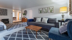 Un salon avec un canapé, une table basse et un tapis à motifs. Des tableaux encadrés ornent le mur, et une lampe se trouve sur une table d’appoint.